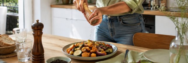 Personne moulant du poivre noir sur un plat de légumes dans une cuisine lumineuse