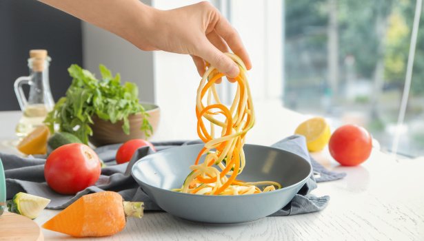 Femme tenant des courgettes fraîches et des spaghettis à la carotte sur un bol