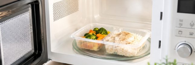 Micro-ondes blanc avec barquette alimentaire en plastique contenant du riz, du poulet et des légumes en cours de réchauffage dans une cuisine lumineuse