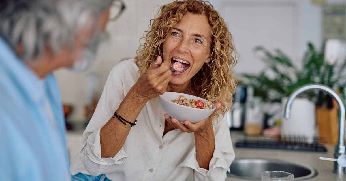 Femme mangeant un bol de céréales et de fruits dans une cuisine, illustrant la chrononutrition et l'importance des horaires des repas.