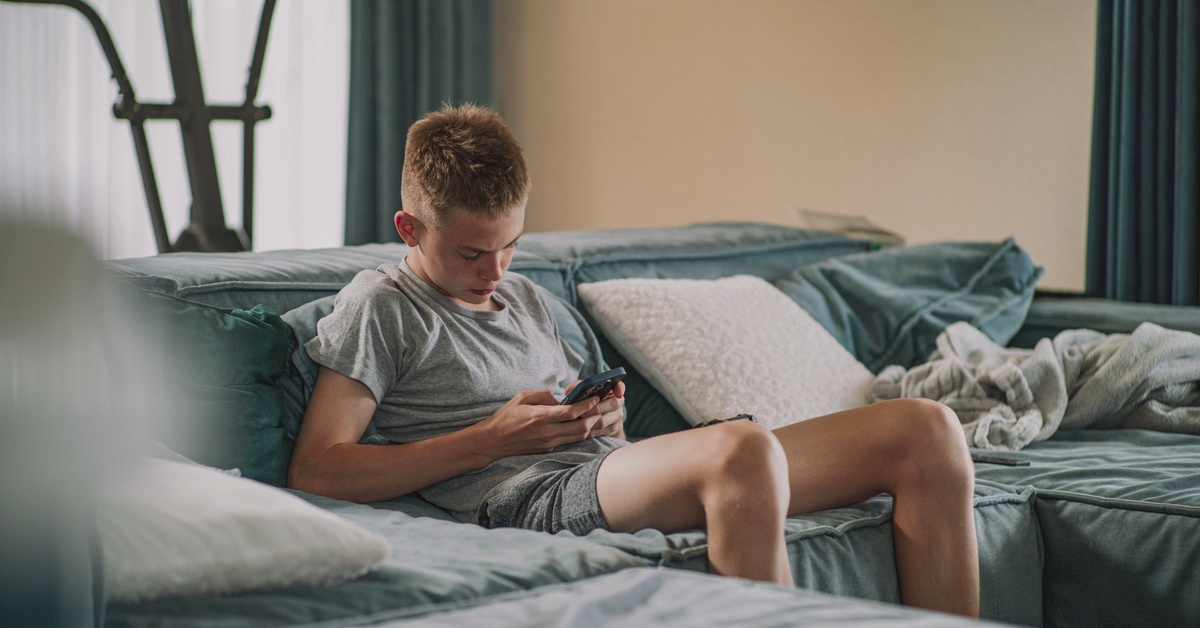 Adolescent assis sur un canapé et concentré sur son smartphone dans un salon.