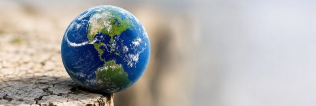 Globe terrestre en équilibre précaire au bord d’un sol sec et fissuré.