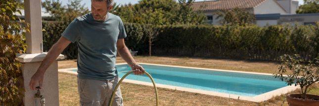 Un homme ferme le robinet d’un tuyau d’arrosage près de sa piscine pendant une période de sécheresse.