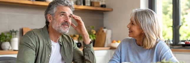 Couple de seniors discutant dans une cuisine, tandis que l’homme cherche ses mots