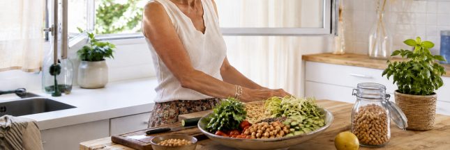 Femme préparant un repas froid avec des pois chiches, des crudités et un blender pendant une journée de forte chaleur.