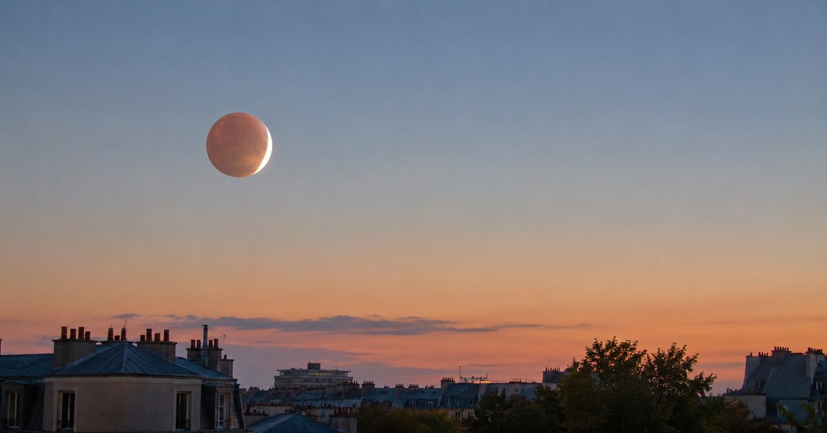 Éclipse lunaire partielle dans le ciel à l'aube au-dessus des toits d'une ville française