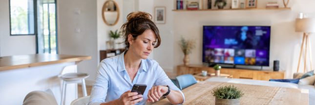 Femme consultant sa montre connectée et son smartphone dans un salon