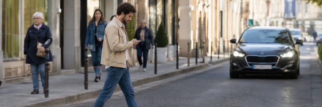 Piéton regardant son smartphone en traversant une rue devant une voiture