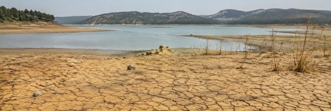 Réservoir presque asséché et sol craquelé sous une forte chaleur, illustrant le dépassement du seuil climatique de 1,5 °C.